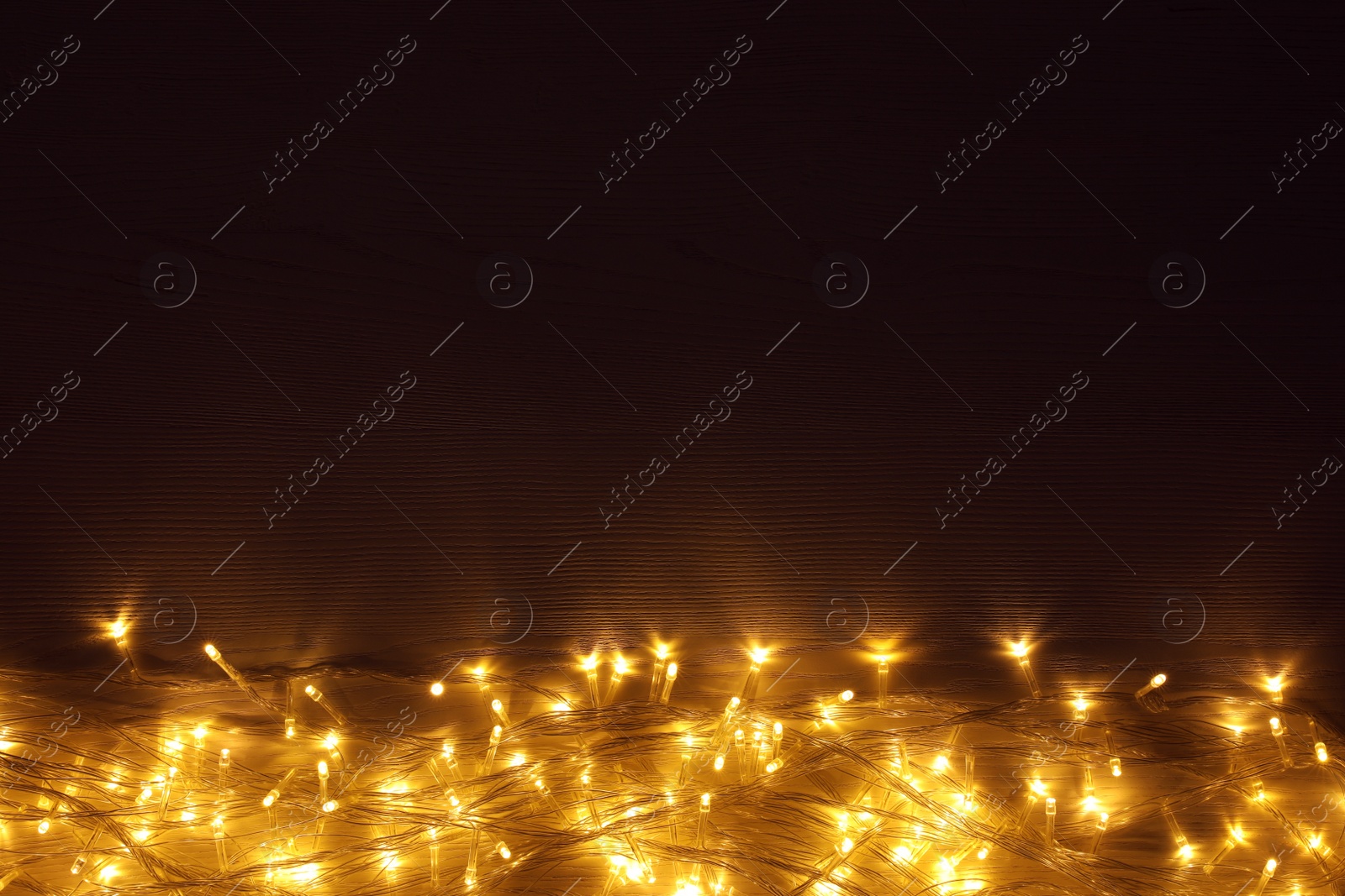 Photo of Beautiful glowing Christmas lights on wooden table, top view. Space for text