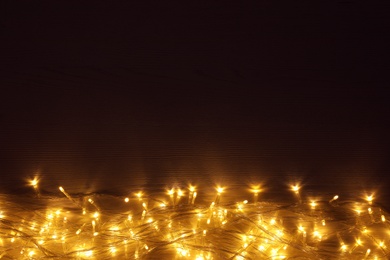 Beautiful glowing Christmas lights on wooden table, top view. Space for text