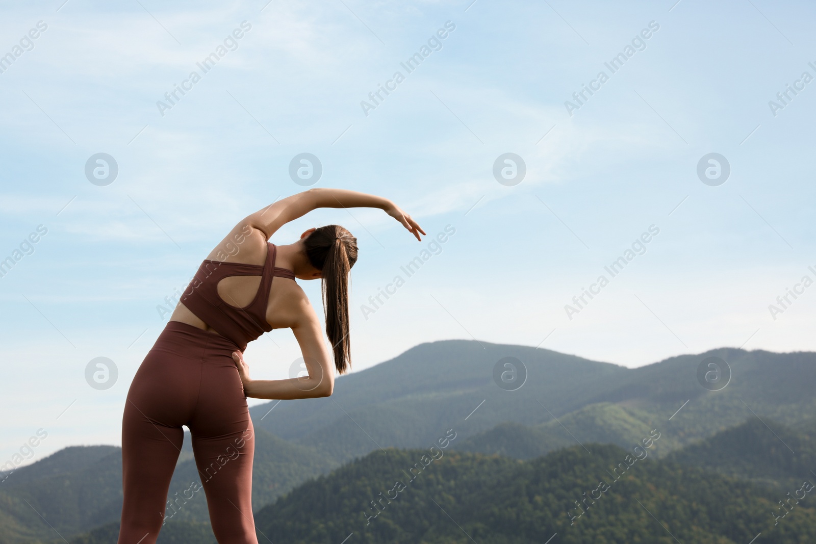 Photo of Woman doing morning exercise in mountains, back view. Space for text