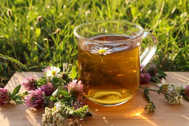 Photo of Cup of aromatic herbal tea and different wildflowers on green grass outdoors, closeup