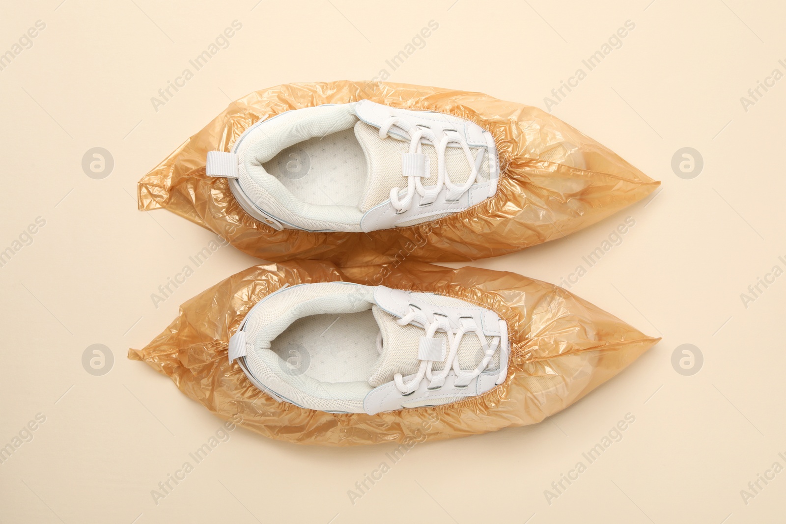 Photo of Sneakers in shoe covers on beige background, top view