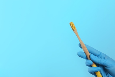 Photo of Dentist holding wooden toothbrush on color background, space for text