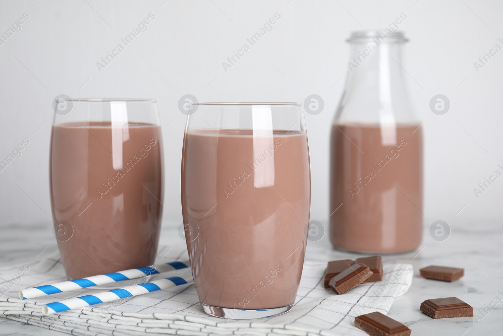 Photo of Delicious chocolate in glasses and bottle of milk on table