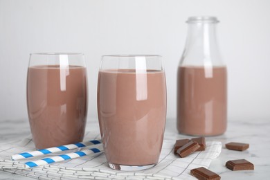 Delicious chocolate in glasses and bottle of milk on table