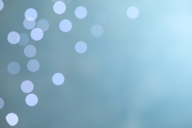 Blurred view of festive lights on light blue background, space for text. Bokeh effect