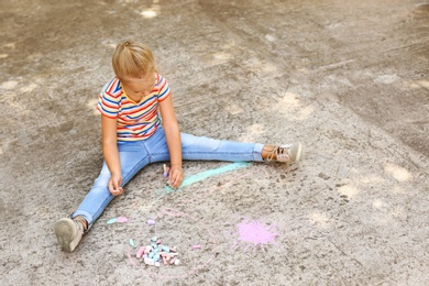 Photo of Cute little left-handed girl drawing with chalk on asphalt