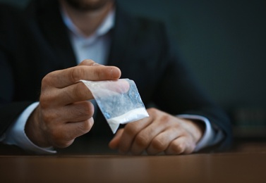 Criminal holding drug at table indoors, closeup