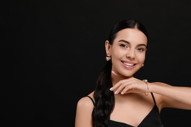 Young woman with elegant pearl jewelry on black background, space for text