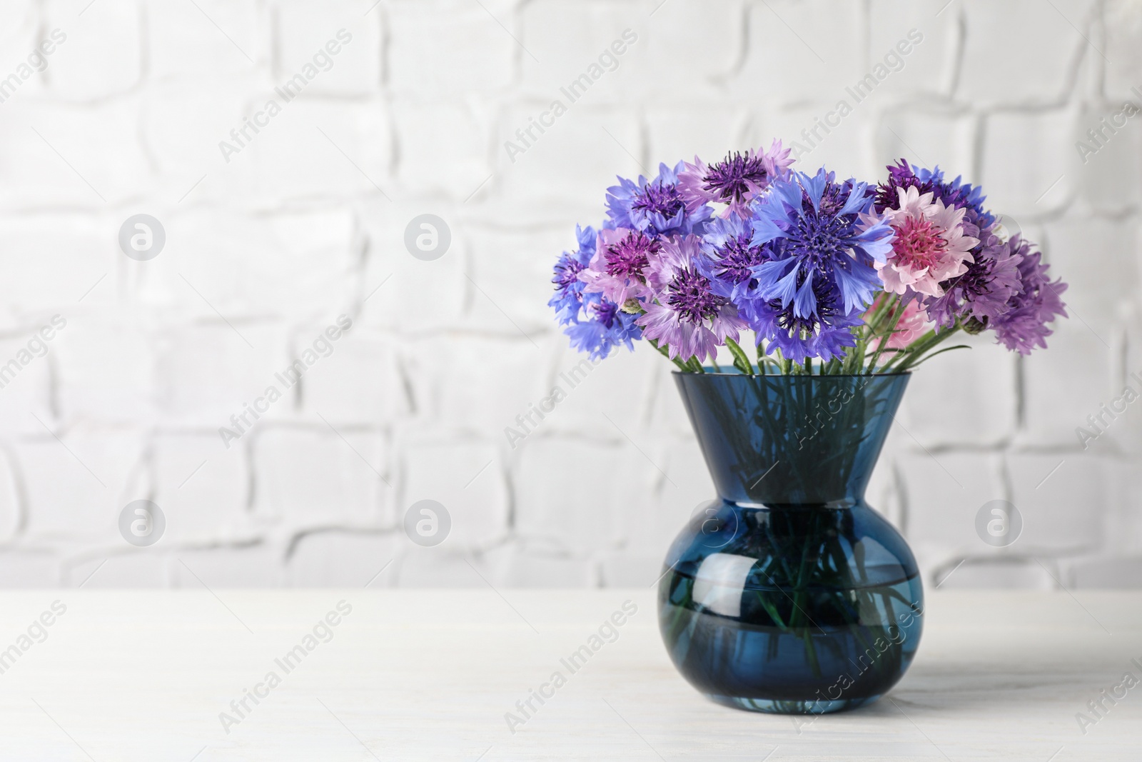 Photo of Bouquet of beautiful cornflowers in glass vase on white wooden table. Space for text