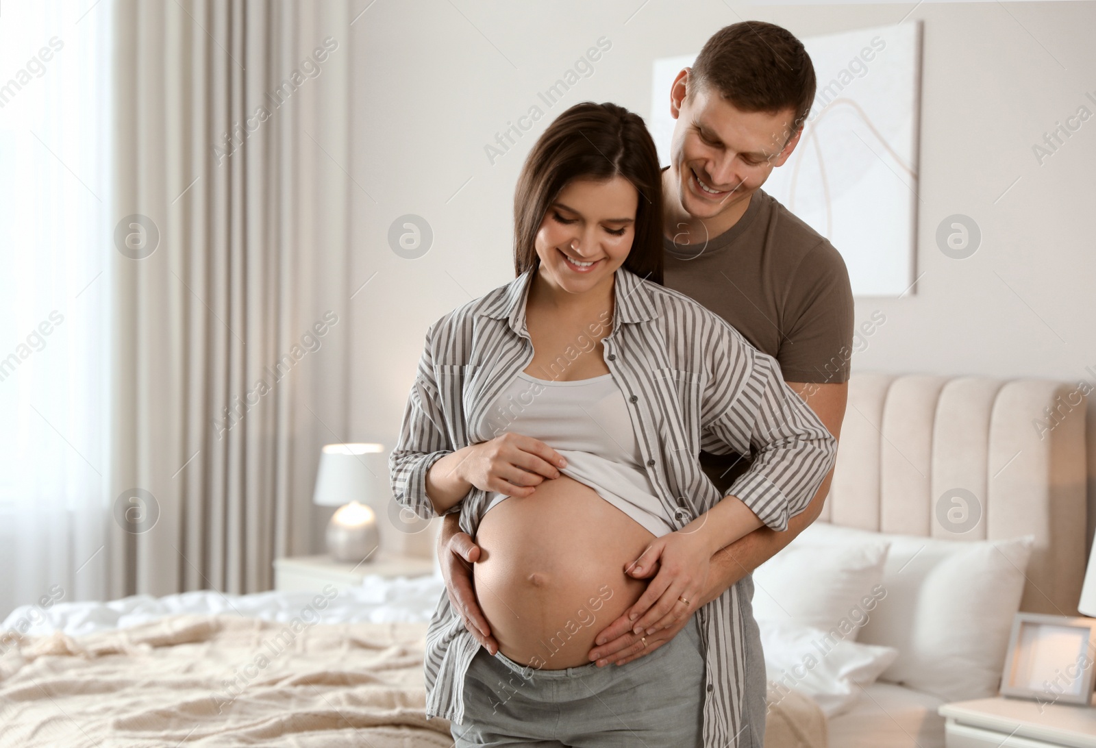 Photo of Young pregnant woman with her husband in bedroom