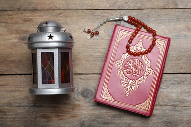 Arabic lantern, quran and misbaha on wooden table, flat lay