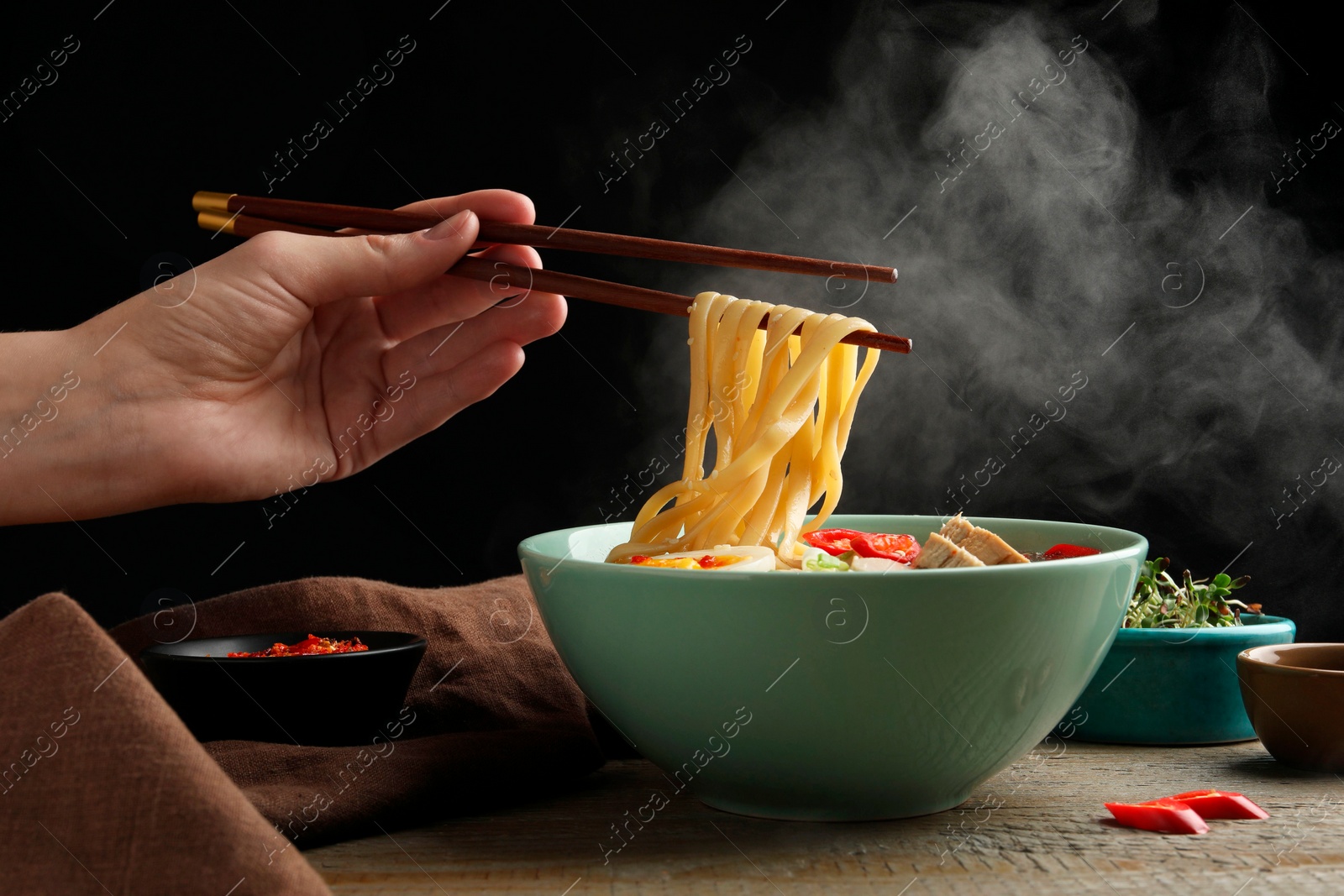 Photo of Woman eating delicious ramen with chopsticks at wooden table, closeup. Noodle soup