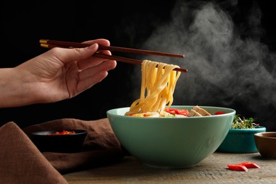 Woman eating delicious ramen with chopsticks at wooden table, closeup. Noodle soup