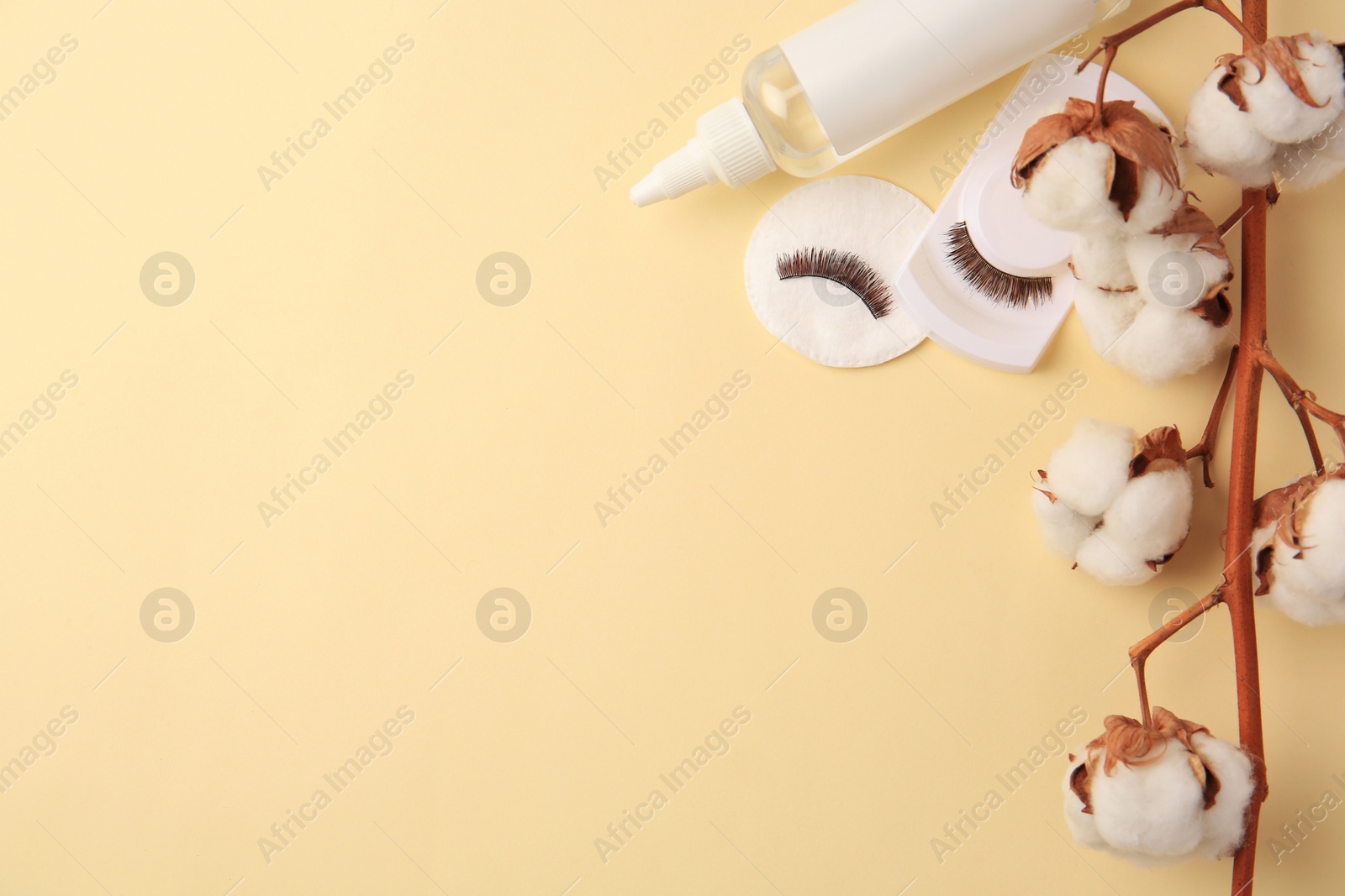 Photo of Bottle of makeup remover, cotton flowers, pad and false eyelashes on yellow background, flat lay. Space for text