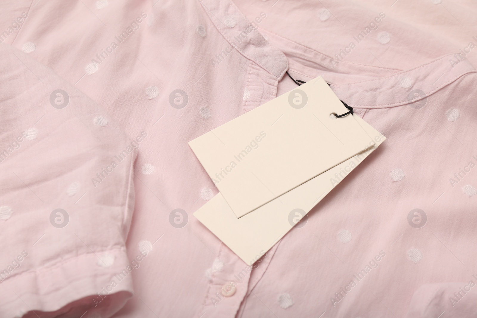 Photo of Blank white tags on light pink shirt with polka dot pattern. Space for text