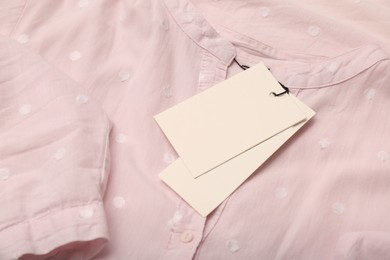 Photo of Blank white tags on light pink shirt with polka dot pattern. Space for text