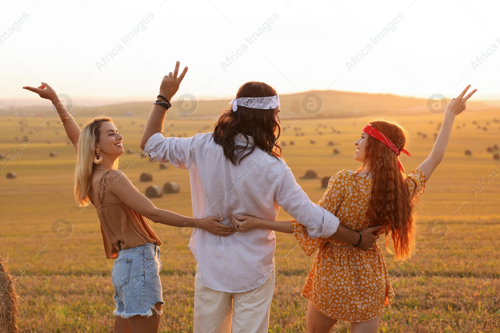 Photo of Happy hippie friends showing peace signs in field, back view