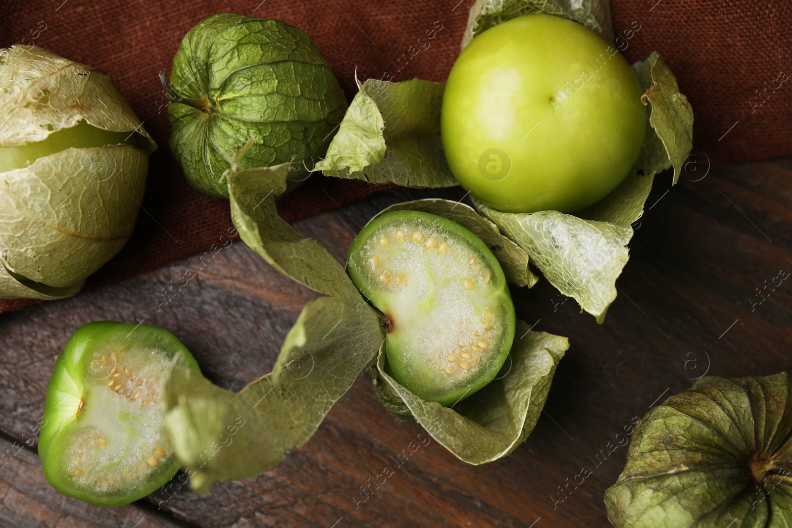 Photo of Fresh green tomatillos with husk on wooden table, flat lay