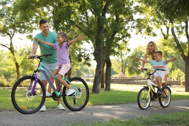 Photo of Happy parents teaching their children to ride bicycle in park