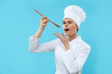 Photo of Emotional female chef with wooden spoon on light blue background