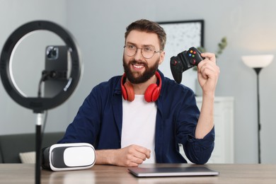 Smiling technology blogger with game controller recording video review at home
