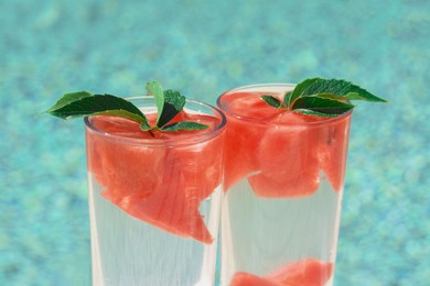 Refreshing watermelon drink in glasses near swimming pool outdoors, closeup