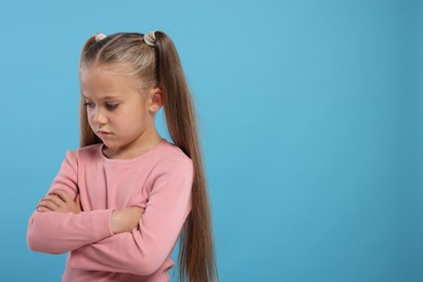 Photo of Resentful girl with crossed arms on light blue background. Space for text