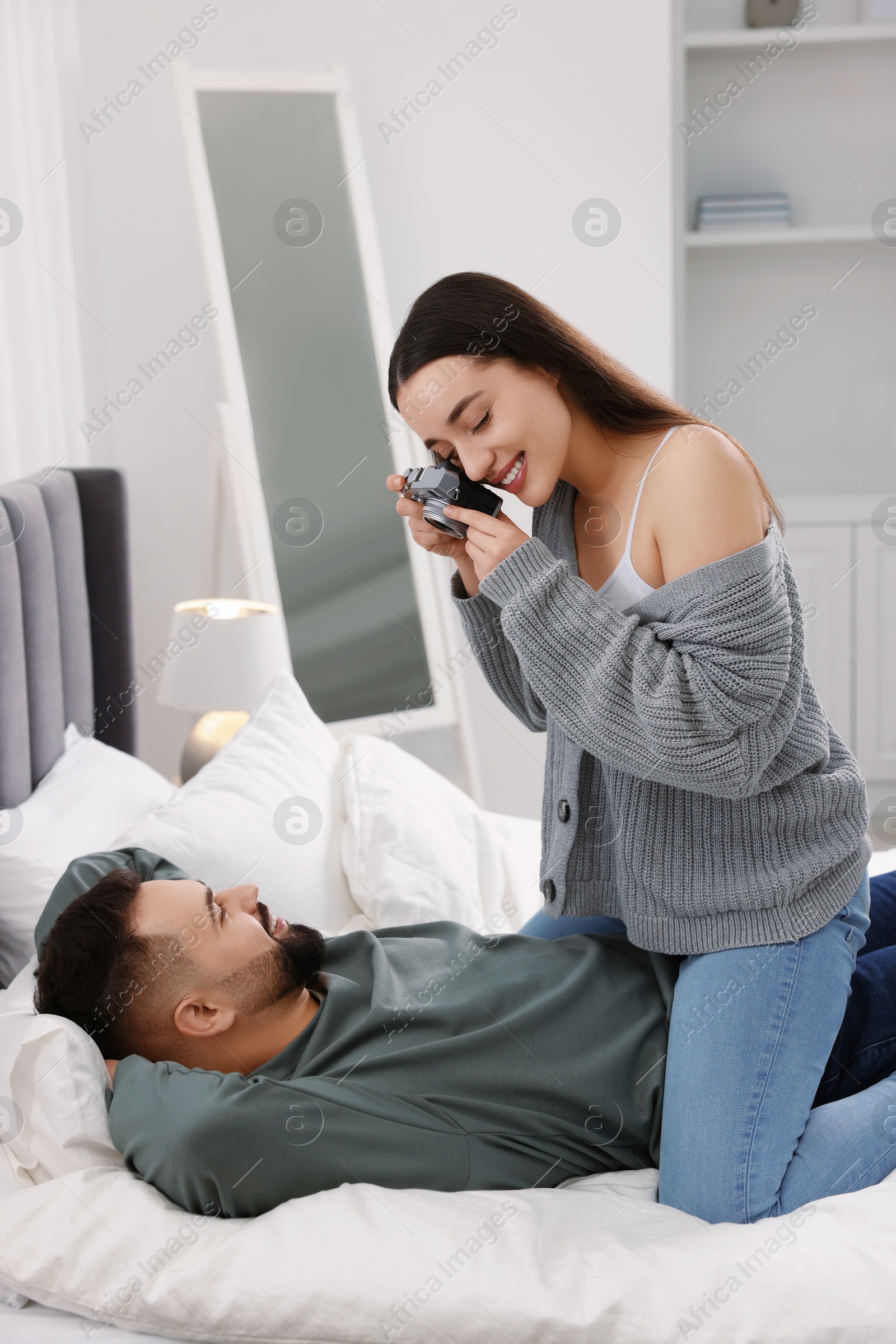 Photo of Happy young couple spending time in bedroom. Smiling woman taking photo of her boyfriend