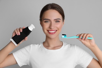 Photo of Young woman holding brush and tube with charcoal toothpaste on grey background