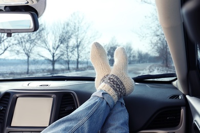 Photo of Young woman in warm socks holding her legs on car dashboard. Cozy atmosphere
