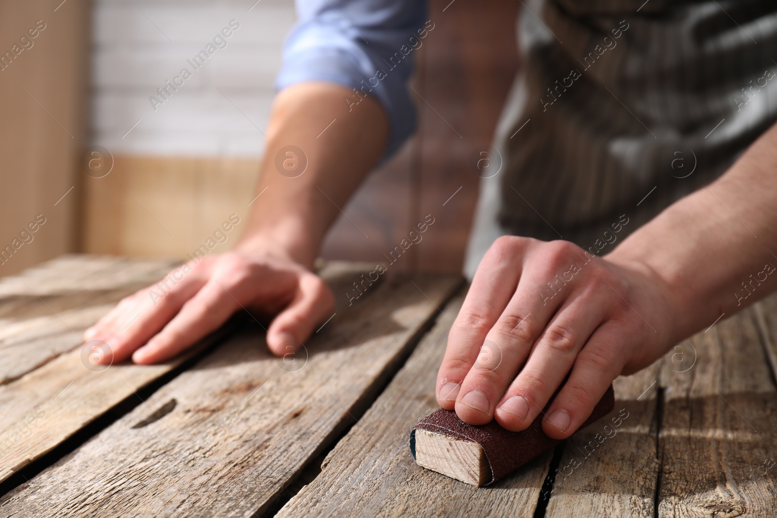 Photo of Man polishing wooden table with sandpaper indoors, closeup