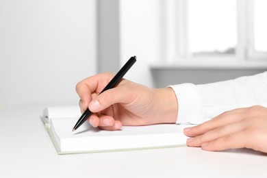 Woman writing in notebook at white table in office, closeup