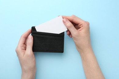 Photo of Woman holding business card holder with blank card on light blue background, top view