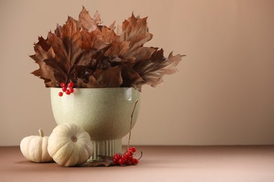 Photo of Composition with beautiful autumn leaves, berries and pumpkins on table against beige background, space for text