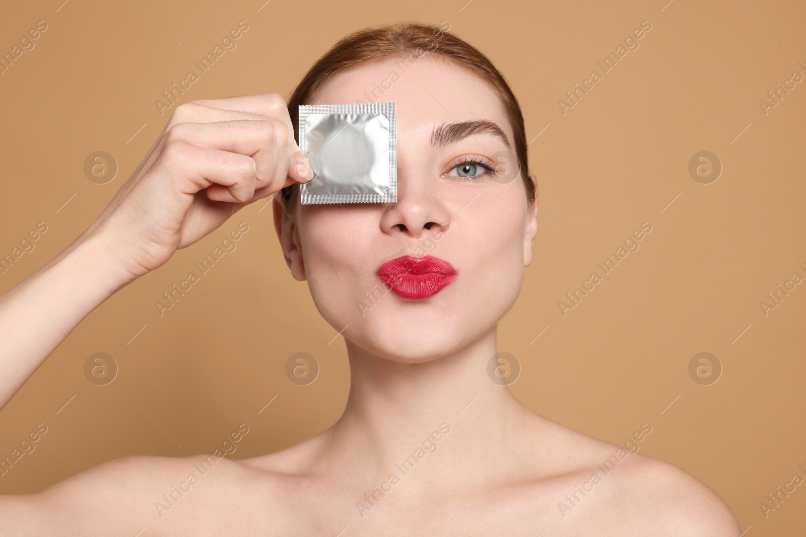 Photo of Woman holding condom on beige background. Safe sex