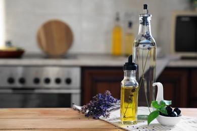 Photo of Different cooking oils, olives, basil and lavender flowers on wooden table in kitchen, space for text