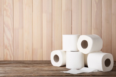 Photo of Rolls of toilet paper on wooden table. Space for text