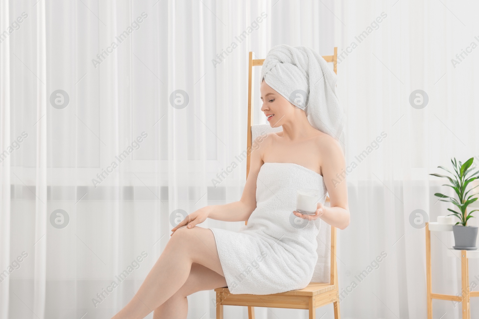 Photo of Beautiful young woman applying body cream onto leg indoors