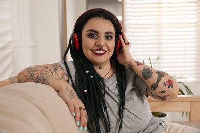 Photo of Beautiful young woman with tattoos on body, nose piercing and dreadlocks listening to music at home