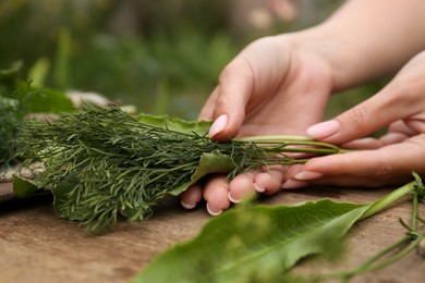 Photo of Woman holding fresh green herbs at wooden table, closeup