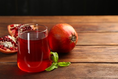 Photo of Tasty pomegranate juice in glass and fresh fruits on wooden table, closeup. Space for text