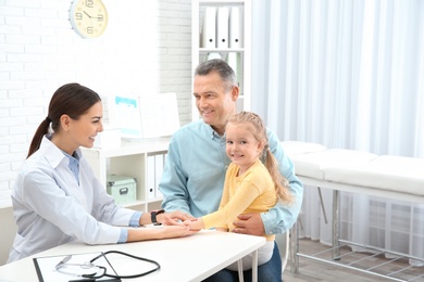 Mature man with granddaughter visiting doctor in hospital, space for text. Checking pulse