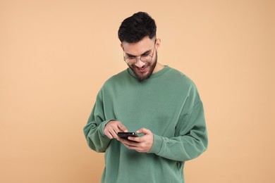 Happy young man using smartphone on beige background