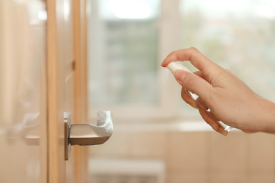 Photo of Woman spraying antiseptic onto door handle indoors, closeup