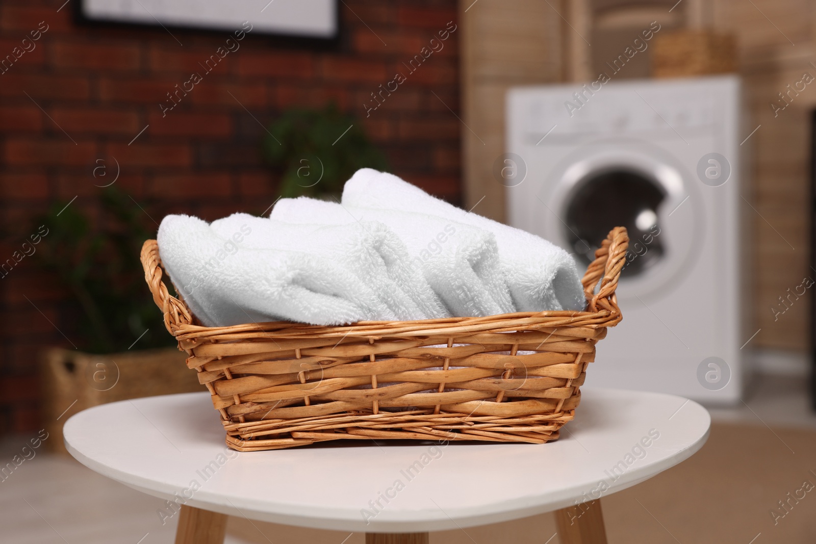 Photo of Wicker basket with folded towels on white table in laundry room