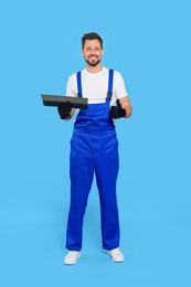 Professional worker with putty knife on light blue background