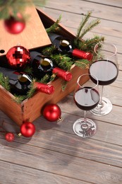 Photo of Wooden crate with bottles of wine, glasses, fir twigs and red Christmas balls on table