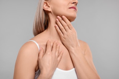 Woman touching her neck on grey background, closeup