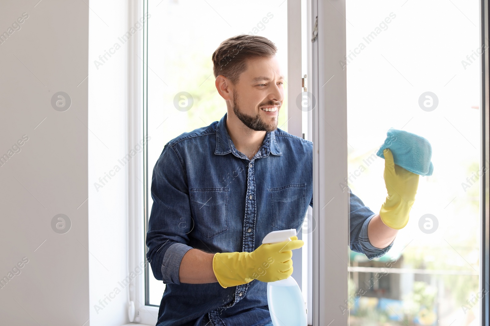 Photo of Man in casual clothes washing window glass at home