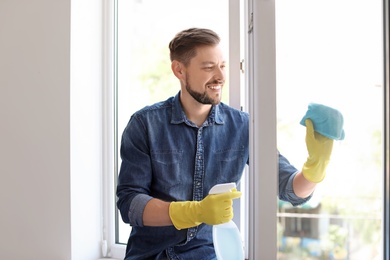 Man in casual clothes washing window glass at home